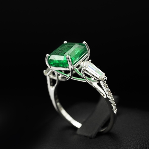 144 - AN 18CT WHITE GOLD EMERALD AND DIAMOND RING, set with an octagonal cut central emerald, flanked by t... 