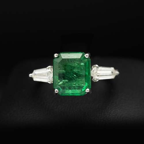 144 - AN 18CT WHITE GOLD EMERALD AND DIAMOND RING, set with an octagonal cut central emerald, flanked by t... 