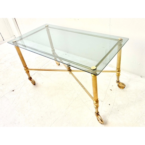80 - REGENCY STYLE GILT METAL LOW TABLE. with a glass top on x-frame stretchered supports and castors.