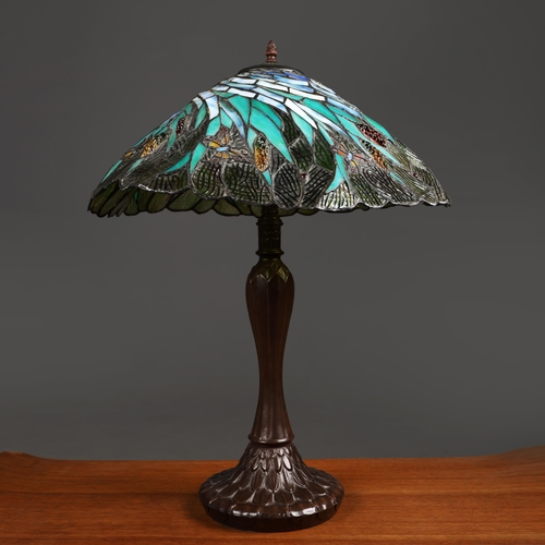 128 - TIFFANY STYLE TABLE LAMP. the shade with a swirling stylised foliage design, bronzed base, raised on... 
