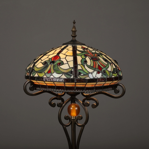 132 - TIFFANY STYLE FLOOR LAMP. the glass shade in a symmetrical stylised foliage design, raised on a scro... 