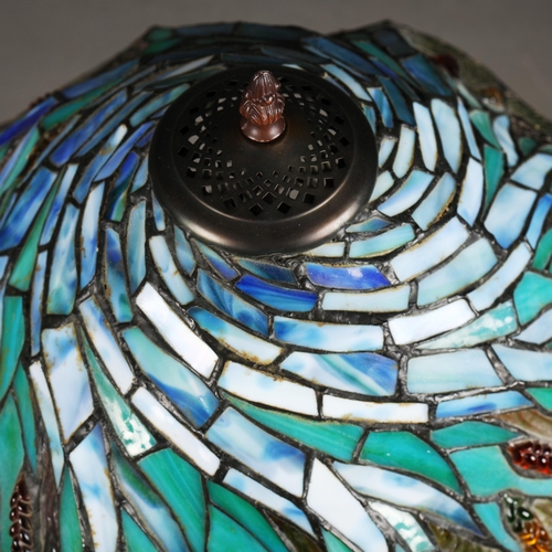 128 - TIFFANY STYLE TABLE LAMP. the shade with a swirling stylised foliage design, bronzed base, raised on... 