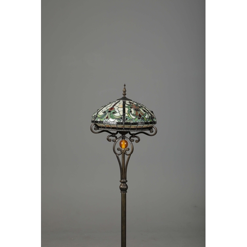 132 - TIFFANY STYLE FLOOR LAMP. the glass shade in a symmetrical stylised foliage design, raised on a scro... 