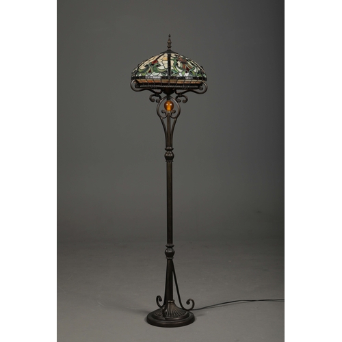 132 - TIFFANY STYLE FLOOR LAMP. the glass shade in a symmetrical stylised foliage design, raised on a scro... 