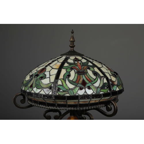 132 - TIFFANY STYLE FLOOR LAMP. the glass shade in a symmetrical stylised foliage design, raised on a scro... 