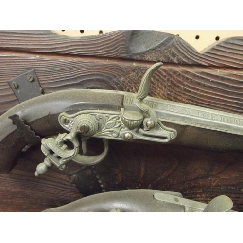 21 - Two reproduction flintlock pistols, mounted on a rustic pine board with steel hooks.