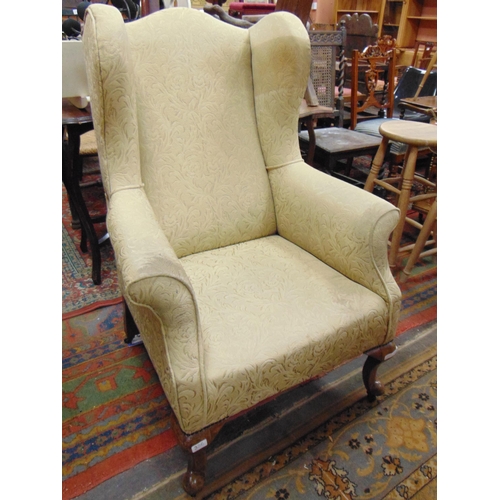 336 - Stout form wingback armchair, set on short turned cabriole supports.