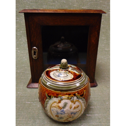 33 - An oak brass mounted smoker's cabinet, having single glazed door, and majolica type tobacco jar. (af... 