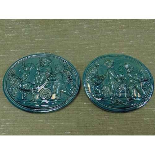 131 - Pair of antique oval glazed wall plaques, depicting cherubs larking. Each 8