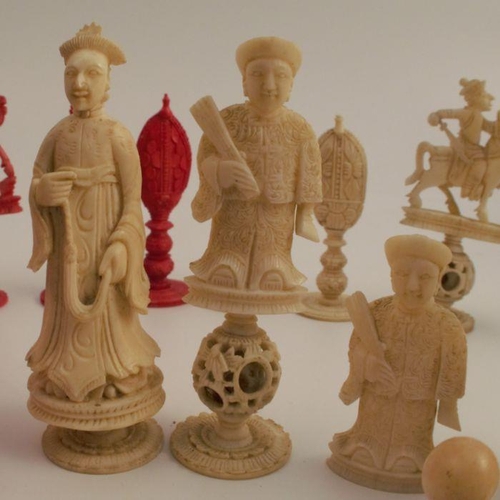 153 - A collection of carved bone chess pieces, some carved with puzzle balls, natural or stained red, in ... 