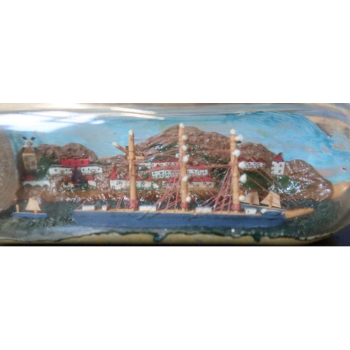 133 - A model ship, in a square shaped bottle, with painted back drop