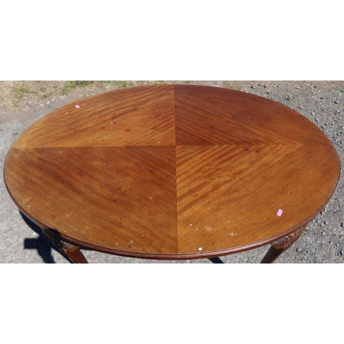 20 - A mahogany quarter veneered oval table, with carved decoration to the scroll leg, terminating in cla... 