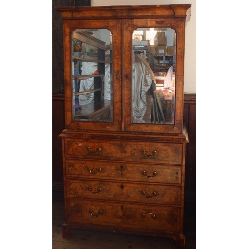 23 - An antique walnut cabinet on chest, the upper section fitted with a pair of mirrored doors, opening ... 