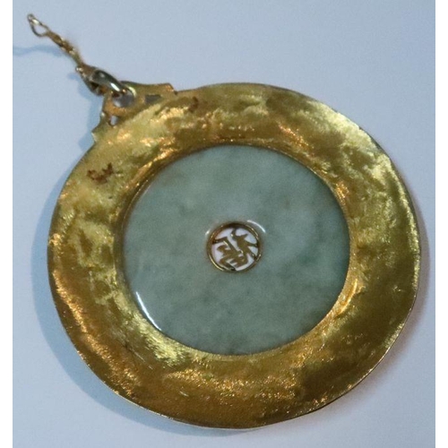 395 - A large jadeite disc pendant, set with characters to the center and mounted in a textured yellow met... 