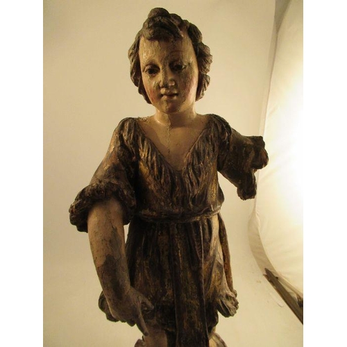 236 - An antique carved wooden polychrome figure of a girl in a gilt dress, standing on a rocky outcrop he... 