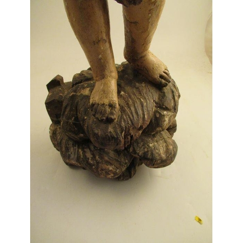 236 - An antique carved wooden polychrome figure of a girl in a gilt dress, standing on a rocky outcrop he... 