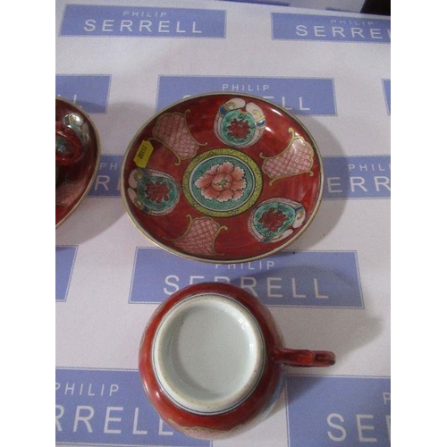 202 - Two Oriental porcelain tea cups and saucers, decorated with panels to the a red ground, with charact... 