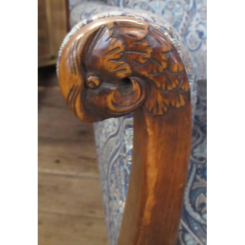 45 - An upholstered and showwood wing armchair, the arms carved with parrots heads