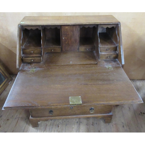 34 - An oak bureau, the fall flap opening to reveal drawers, pigeon holes and a covered well, over two sh... 