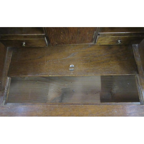 34 - An oak bureau, the fall flap opening to reveal drawers, pigeon holes and a covered well, over two sh... 