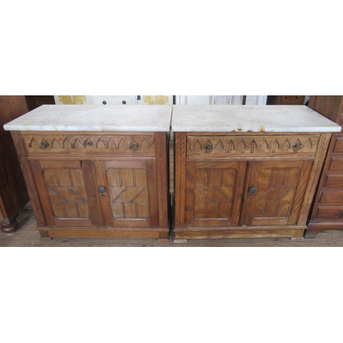 29 - A pair of Edwardian oak and marble topped cabinets, with Gothic style decoration, having a frieze dr... 