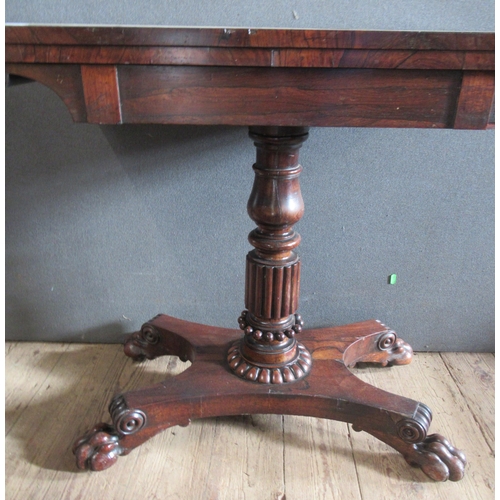 32 - A 19th century rosewood fold over games table, on turned column, to platform base with paw feet, wid... 