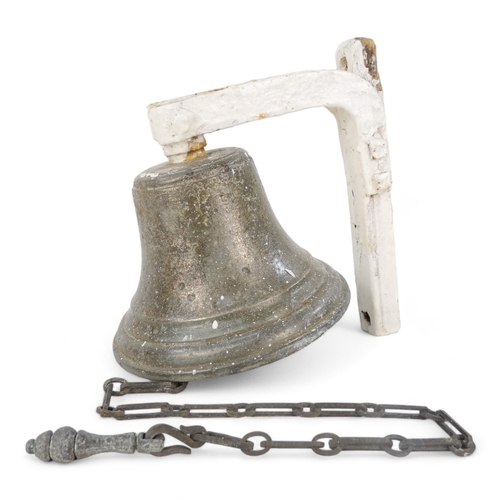 24 - A vintage bronze bell - with a white painted bracket, 18cm high.