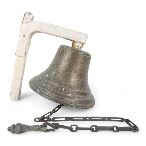 24 - A vintage bronze bell - with a white painted bracket, 18cm high.