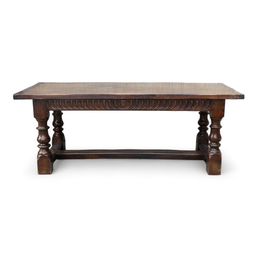 951 - A 17th century style oak refectory table - the cleated plank top above a carved frieze and square an... 