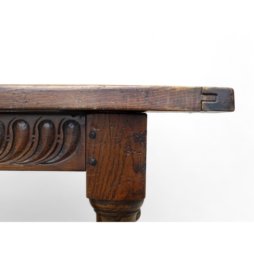 951 - A 17th century style oak refectory table - the cleated plank top above a carved frieze and square an... 