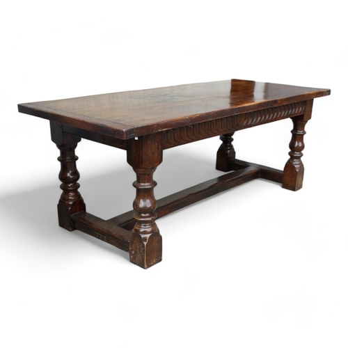 951 - A 17th century style oak refectory table - the cleated plank top above a carved frieze and square an... 