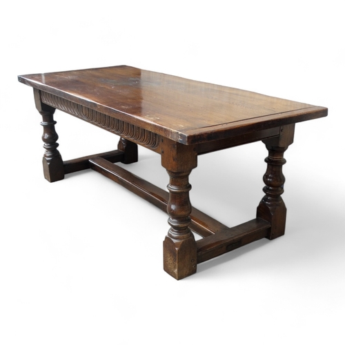 951 - A 17th century style oak refectory table - the cleated plank top above a carved frieze and square an... 