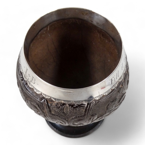 54 - An 18th century silver mounted coconut cup - the bowl carved with hunting figures and a musician, th... 