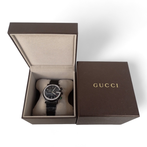 712 - A Gucci chronograph wristwatch - the black steel case with diamond G bezel, boxed with papers.