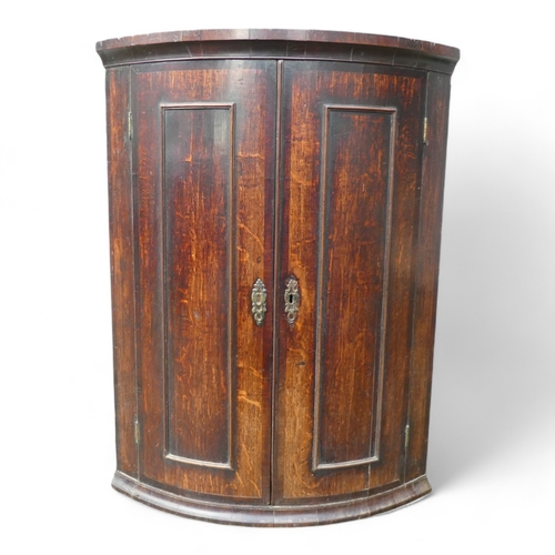 961 - A George III oak and mahogany inlaid bowfront corner cupboard - the moulded cornice above a pair of ... 