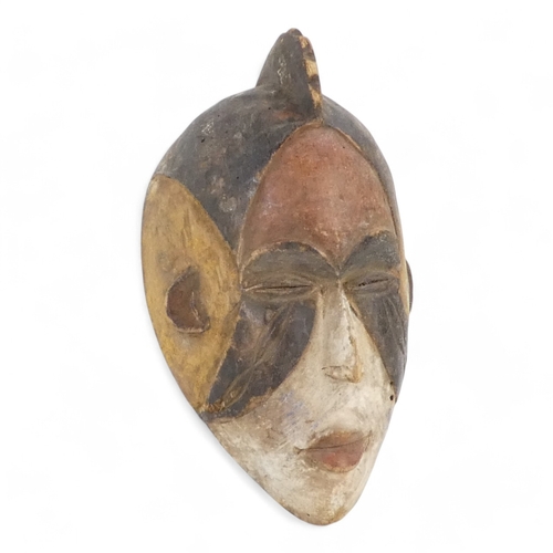 115 - A polychrome painted tribal African mask - in red, white and umber, with a comb headdress, 25cm high... 