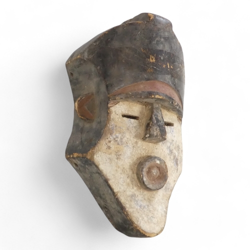 121 - A polychrome painted African mask - the head-dress with an ochre band, the white face with a pouting... 