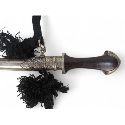 437 - A late 19th century jambiya - the hardwood hilt with white metal mounts and sheath and black woven c... 