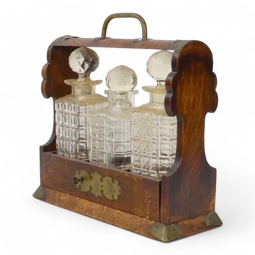 47 - An early 20th century oak tantalus - with brass mounts and three cut glass bottles, 35cm wide.