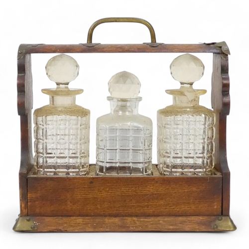 47 - An early 20th century oak tantalus - with brass mounts and three cut glass bottles, 35cm wide.