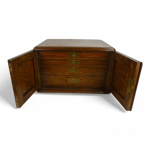 588 - An early 20th century oak canteen - the top incorporating a brass cartouche above a pair of panel do... 