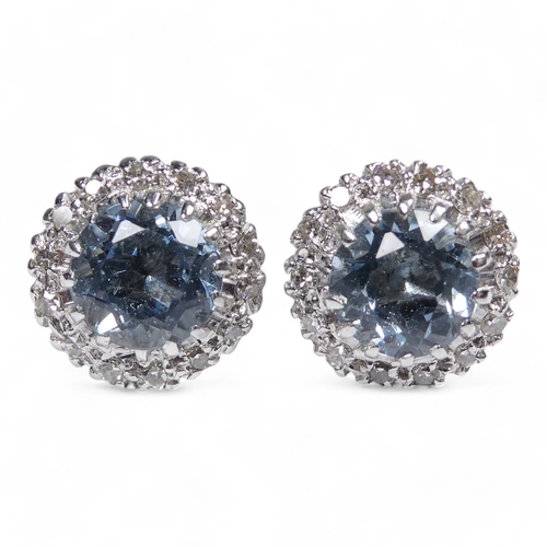 654 - A pair of aquamarine and diamond set ear studs - the central pale blue stones halo set within a band... 