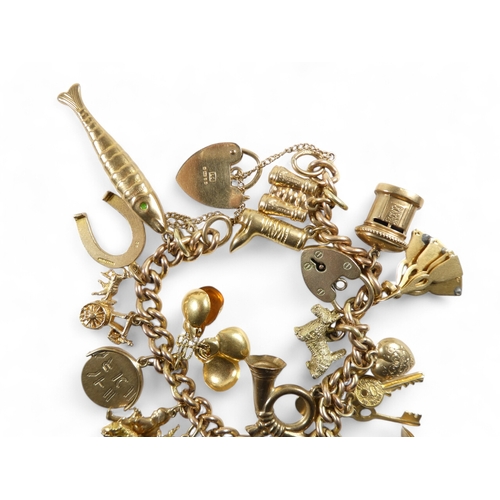 665 - A 9ct gold curb link charm bracelet - with twenty charms mostly marked as 9ct, 49.2g.