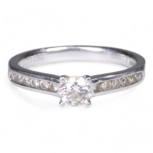 676 - A solitaire diamond ring - on a platinum four claw setting and diamond set shoulders, size M, 4.1g.