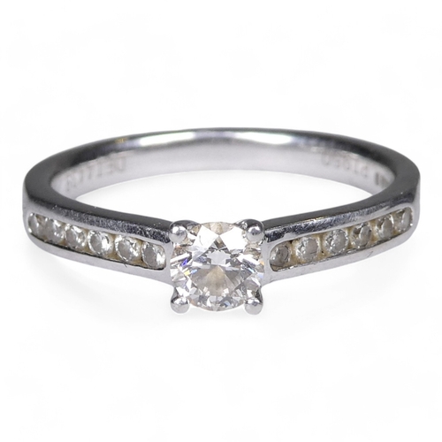 676 - A solitaire diamond ring - on a platinum four claw setting and diamond set shoulders, size M, 4.1g.