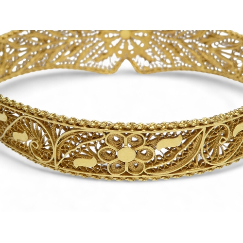 687 - A yellow metal filigree bangle - hinged and of foliate form, indistinctly marked, 24.7g.