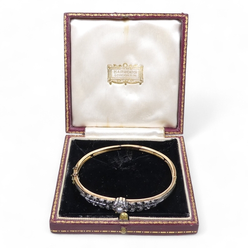 691 - A diamond and pearl set bangle - the claw set pearl within a band of diamonds flanked by foliage, 13... 