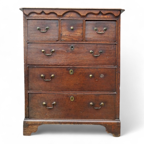 942 - A George III oak chest of drawers - the rectangular top with cusped corners above an arrangement of ... 