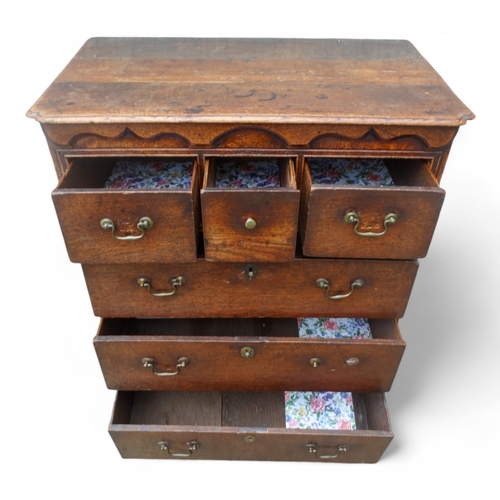 942 - A George III oak chest of drawers - the rectangular top with cusped corners above an arrangement of ... 