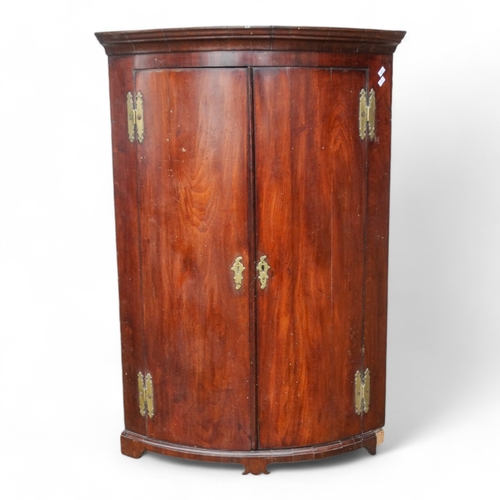 973 - A George III mahogany bowfront corner cupboard - the moulded cornice above a pair of doors enclosing... 